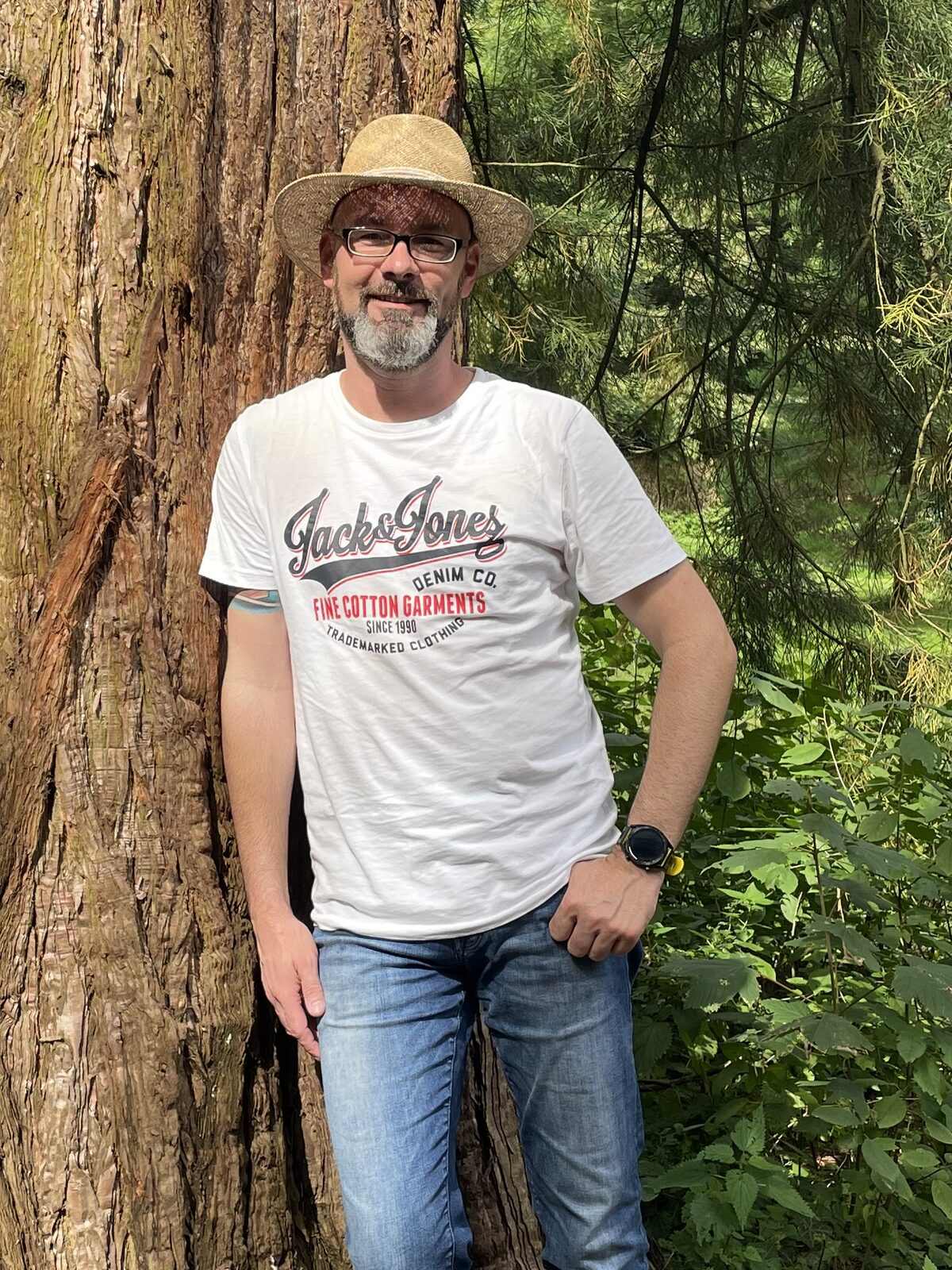 Michael Hohmann mit Strohhut, angelehnt an einen mächtigen Baumstamm